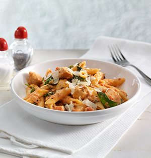 Chicken and Penne in Creamy Vodka Rose Sauce in a white pasta bowl sitting on top of white linens.