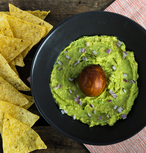 Guacamole made with Astro yogurt served in a black bowl with nacho chips on the side