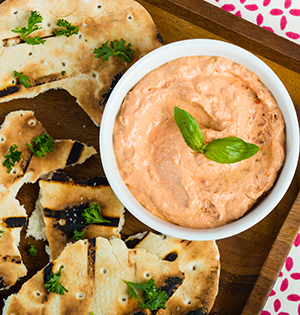 Sun-dried Tomato Yogurt Herb Spread made with Astro yogurt served in a white bowl with grilled pita on the side