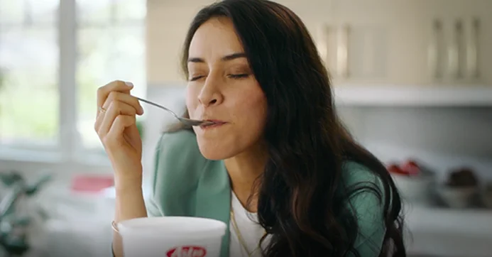 Lady eating a spoonful of Astro yogurt in the kitchen form an Astro yogurt tub