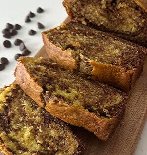 Sliced Chocolate Marble Yogurt Loaf sitting on a wooden cutting board with chocolate chips in the background.