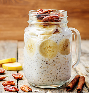 Overnight Oats made with Astro Yogurt in a mason jar sitting on top of a wooden table with pecans and cinnamon sticks.